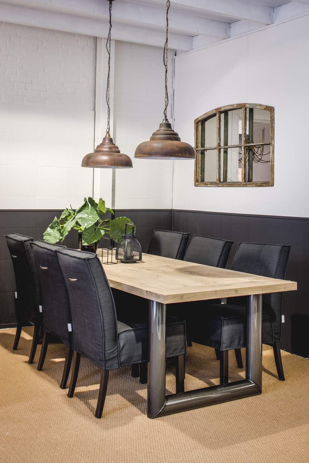 Rectangular dining table with a light wooden top, black chairs and two pendant lamps in the dining area.