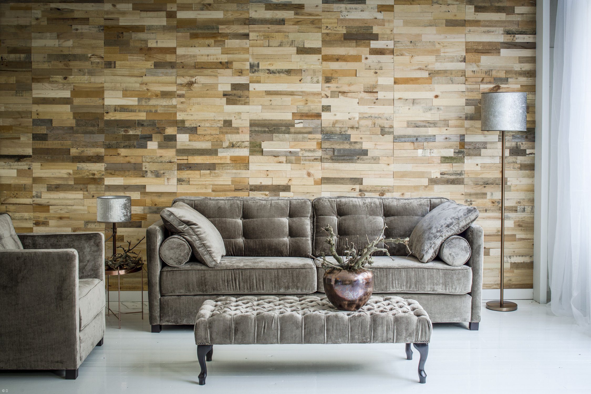 A grey velvet sofa with an upholstered bench in front of a wall of wooden slats.