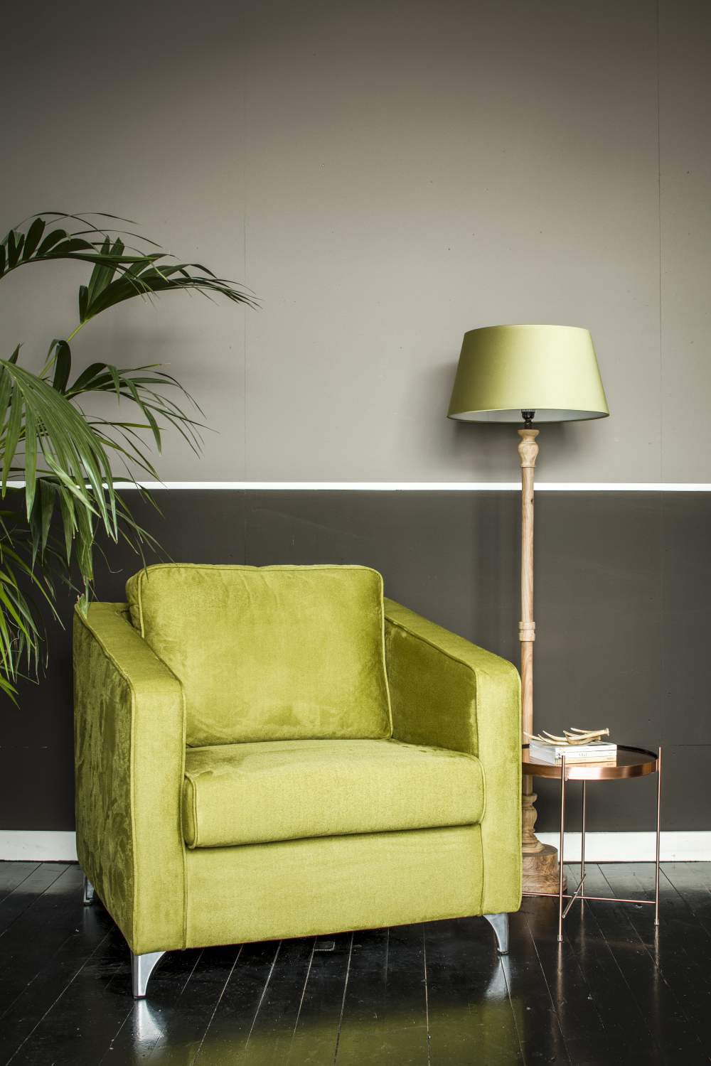 Lichtgroene gestoffeerde fauteuil naast een staande lamp en een klein rond bijzettafeltje voor een tweekleurige muur.