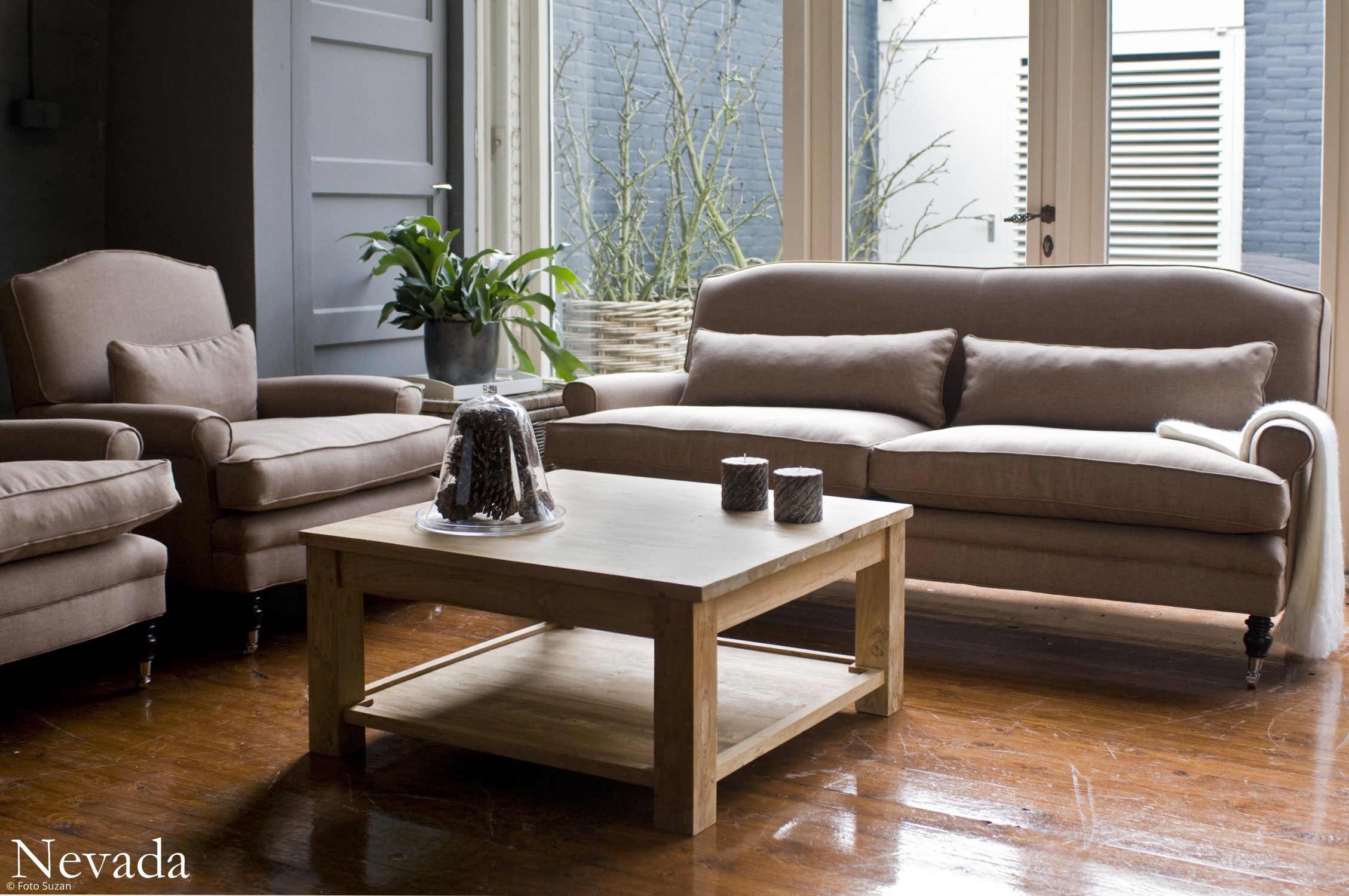 Beige sofagruppe med sofa og lænestole står omkring et lyst sofabord i træ i en lysfyldt stue.