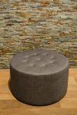 Round upholstered footstool in front of a natural stone wall